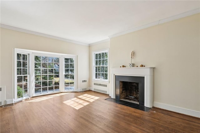 unfurnished living room featuring wood finished floors, a fireplace with flush hearth, baseboards, radiator, and crown molding