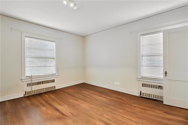spare room featuring baseboards, wood finished floors, rail lighting, and radiator