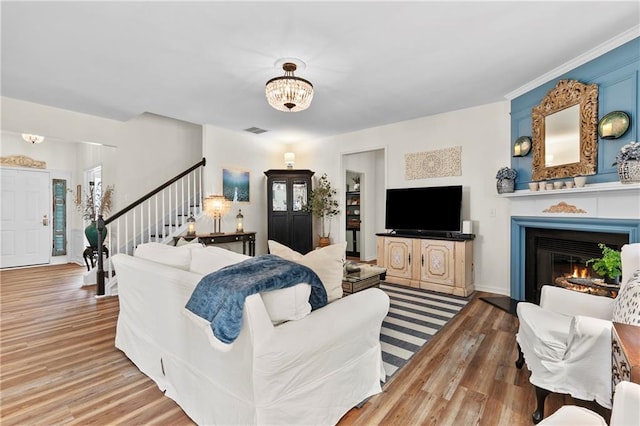 living room with a chandelier, a glass covered fireplace, wood finished floors, visible vents, and stairway