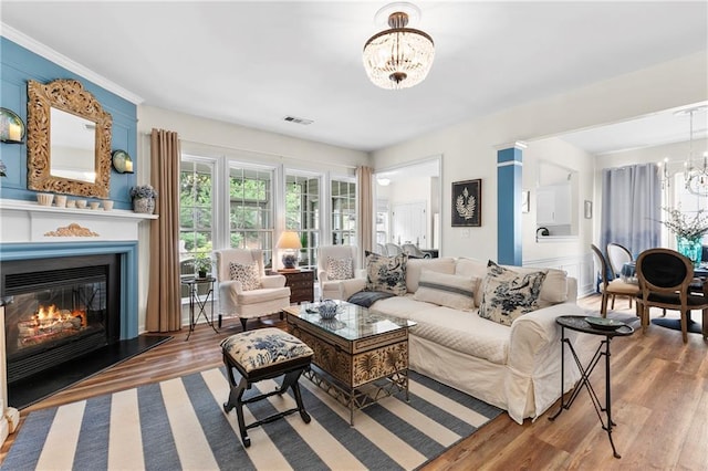 living area with visible vents, a glass covered fireplace, wood finished floors, and a chandelier