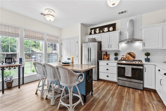 kitchen with wall chimney range hood, plenty of natural light, stainless steel appliances, and white cabinetry
