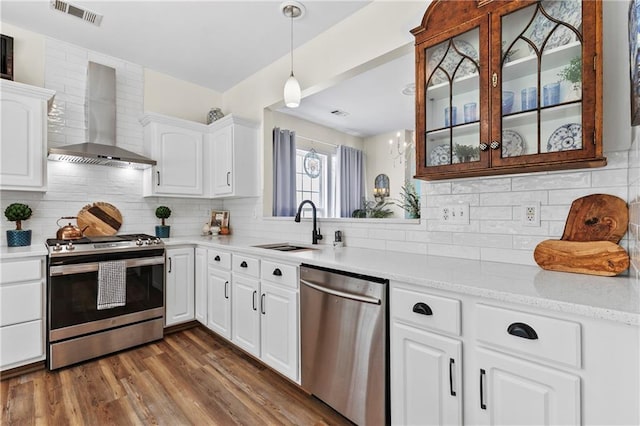kitchen featuring a sink, wall chimney exhaust hood, stainless steel appliances, visible vents, and glass insert cabinets