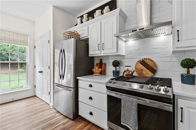 kitchen featuring wall chimney range hood, tasteful backsplash, white cabinets, light wood-style floors, and stainless steel appliances