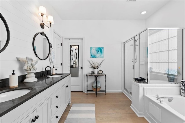 full bath featuring a garden tub, double vanity, wood finished floors, a sink, and a stall shower