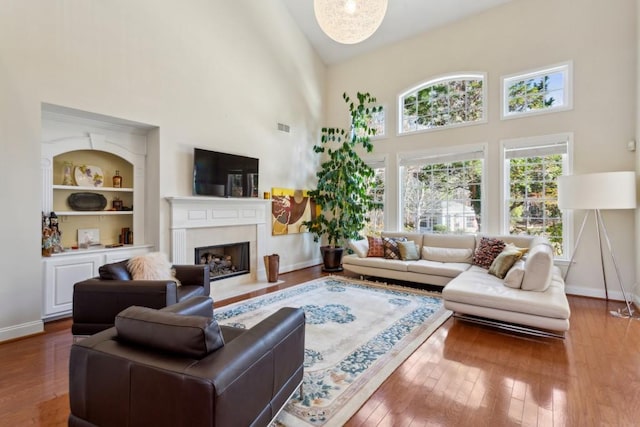 living room with wood-type flooring, built in features, and a high ceiling