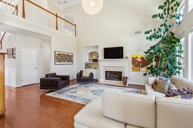 living room featuring hardwood / wood-style flooring, ornamental molding, built in shelves, and a high ceiling