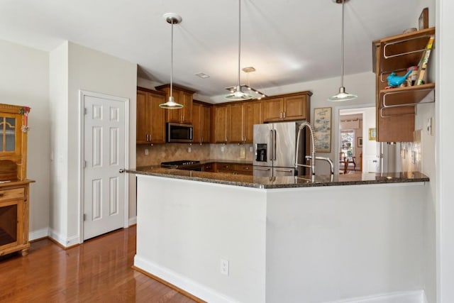 kitchen with hanging light fixtures, appliances with stainless steel finishes, kitchen peninsula, dark stone counters, and backsplash