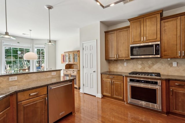 kitchen with decorative light fixtures, wood-type flooring, dark stone countertops, backsplash, and stainless steel appliances