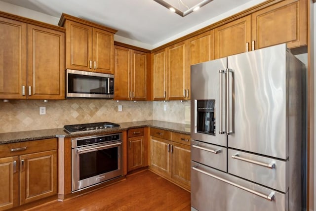 kitchen featuring tasteful backsplash, appliances with stainless steel finishes, dark wood-type flooring, and dark stone counters