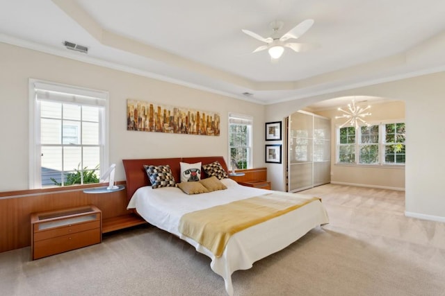 carpeted bedroom featuring a raised ceiling, ornamental molding, and ceiling fan with notable chandelier