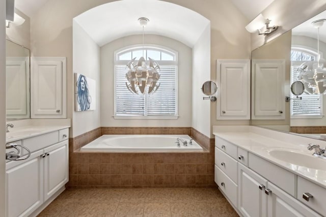 bathroom featuring vanity, vaulted ceiling, tiled bath, and an inviting chandelier