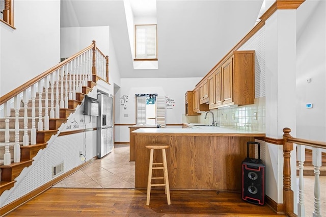1732 Winding Woods Ln, Jonesboro, GA 30236 - kitchen with a towering ceiling, a peninsula, stainless steel refrigerator with ice dispenser, hardwood / wood-style floors, and brown cabinets