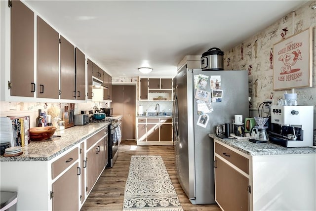 kitchen with tasteful backsplash, sink, light stone counters, light hardwood / wood-style floors, and stainless steel appliances