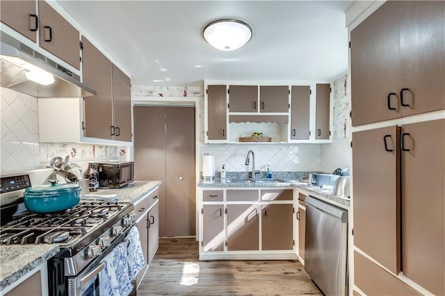 kitchen featuring sink, tasteful backsplash, light stone counters, light wood-type flooring, and appliances with stainless steel finishes