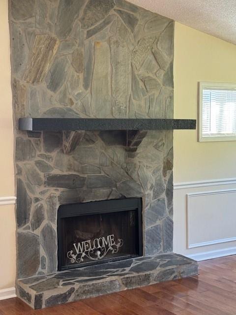 room details featuring a textured ceiling, a stone fireplace, and wood finished floors