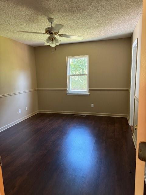 unfurnished room featuring a textured ceiling, a ceiling fan, baseboards, dark wood-type flooring, and visible vents
