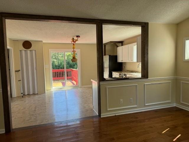 kitchen featuring a textured ceiling, dark wood finished floors, freestanding refrigerator, white cabinetry, and decorative light fixtures