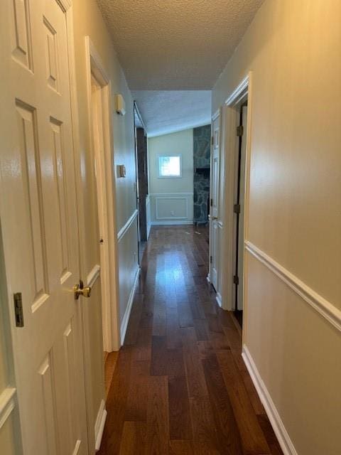 hallway featuring a textured ceiling, a decorative wall, dark wood-style floors, and a wainscoted wall