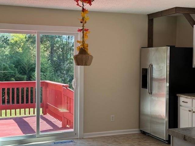 interior space with stainless steel fridge with ice dispenser, baseboards, and white cabinetry