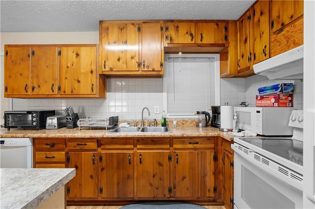 kitchen featuring white appliances, under cabinet range hood, light countertops, and a sink