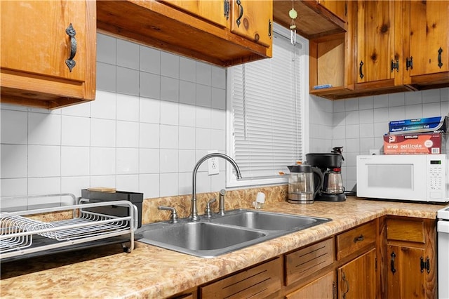 kitchen featuring white microwave, light countertops, a sink, and brown cabinetry