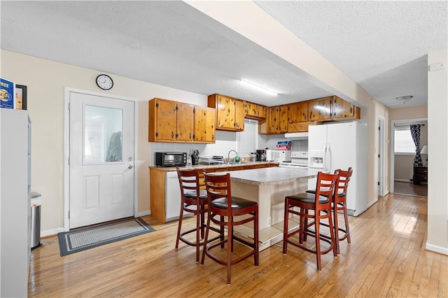 kitchen featuring white appliances, a kitchen island, light countertops, light wood-type flooring, and brown cabinetry