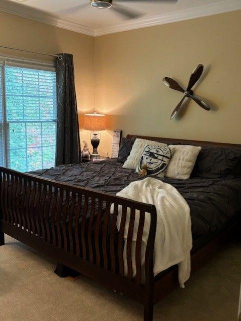 carpeted bedroom with ceiling fan and ornamental molding