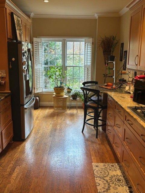 kitchen featuring stone counters, appliances with stainless steel finishes, ornamental molding, and hardwood / wood-style floors