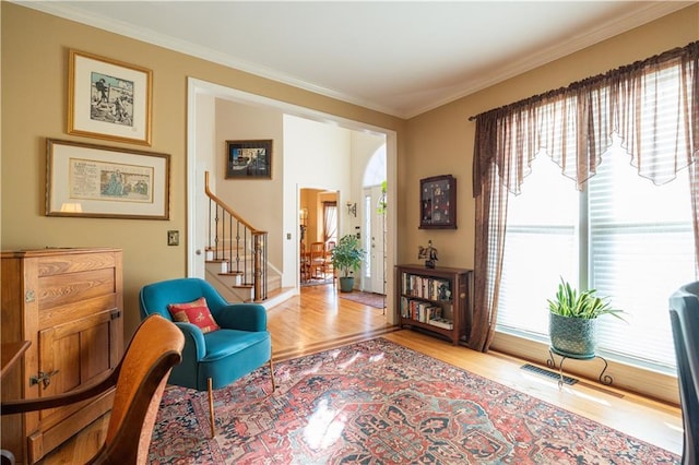 sitting room featuring wood finished floors, crown molding, and stairway