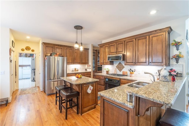 kitchen with appliances with stainless steel finishes, a sink, a breakfast bar area, light stone countertops, and brown cabinetry