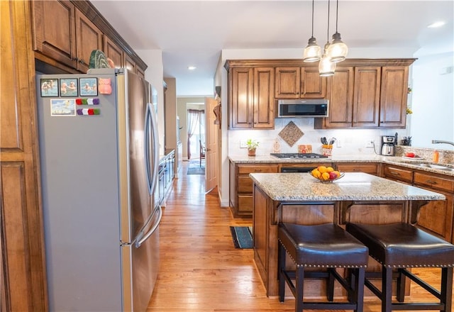 kitchen featuring appliances with stainless steel finishes, light wood-type flooring, brown cabinets, light stone countertops, and recessed lighting