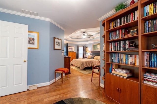 bedroom with light wood-style floors, baseboards, ornamental molding, and a tray ceiling