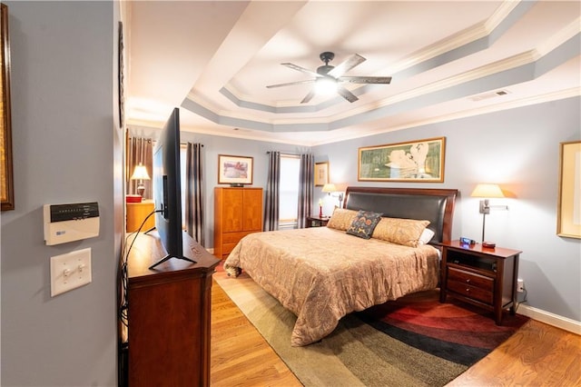 bedroom with a raised ceiling, crown molding, wood finished floors, baseboards, and ceiling fan