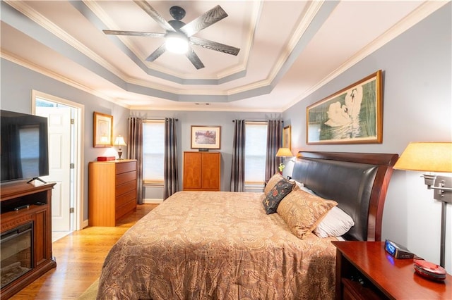 bedroom featuring wood finished floors, ornamental molding, a raised ceiling, and a ceiling fan