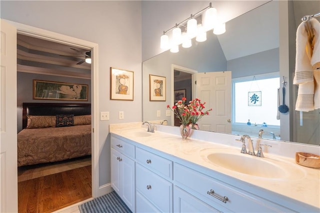 ensuite bathroom with double vanity, wood finished floors, and lofted ceiling