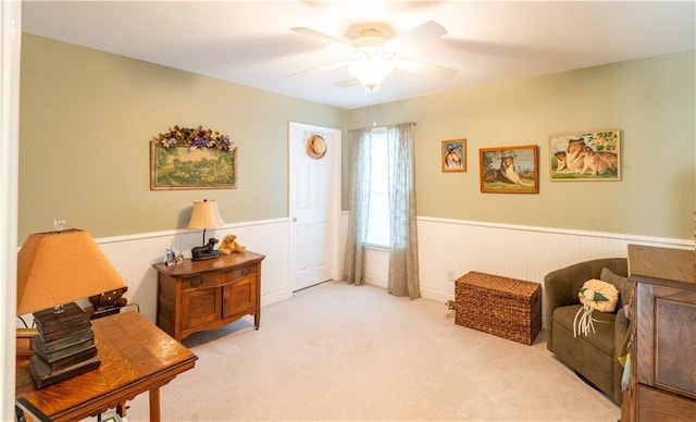 living area with a wainscoted wall, ceiling fan, and carpet floors