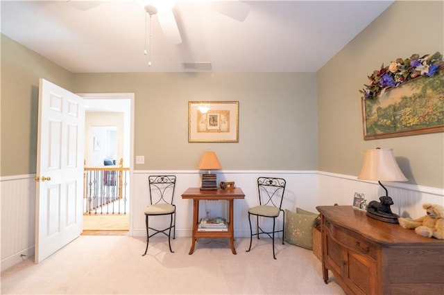 living area featuring a wainscoted wall, carpet floors, and ceiling fan