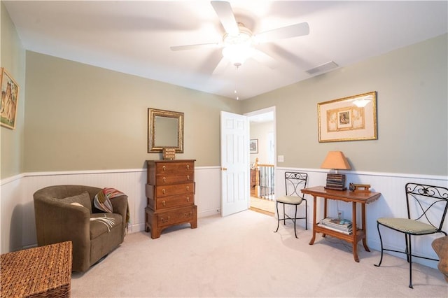 sitting room with wainscoting, a ceiling fan, carpet, and an upstairs landing