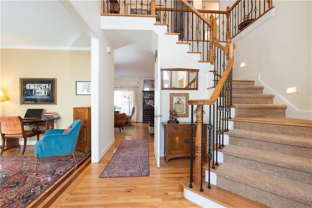 foyer with wood finished floors, stairs, baseboards, and crown molding