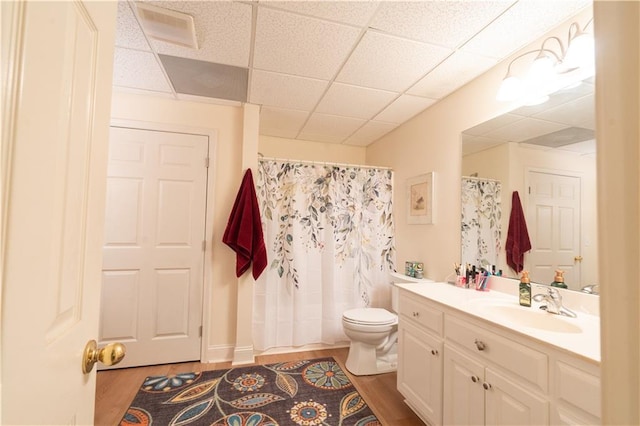 bathroom featuring a paneled ceiling, wood finished floors, toilet, vanity, and curtained shower