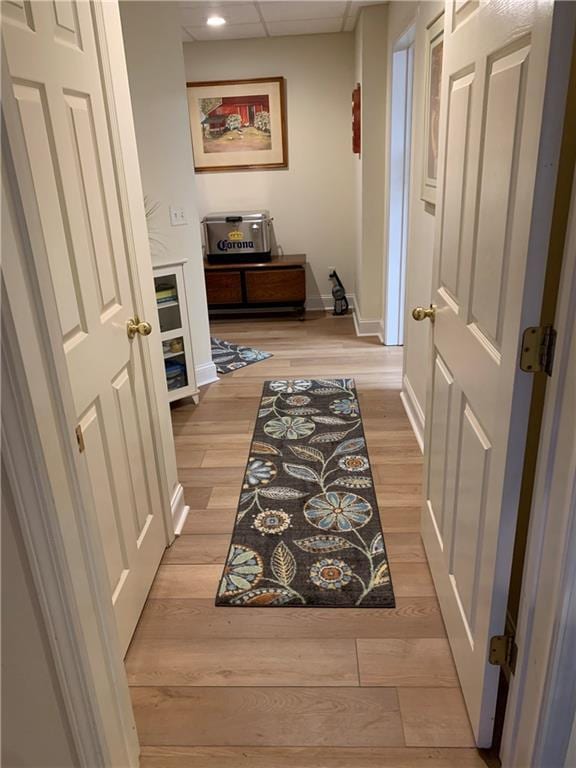 hallway with light wood-style flooring, a paneled ceiling, and baseboards