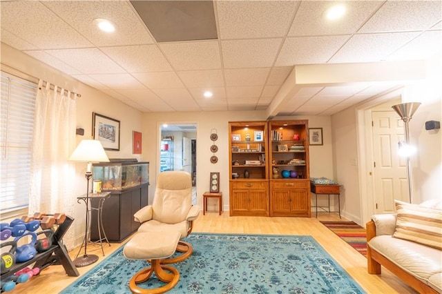 living area featuring light wood-style flooring, baseboards, a paneled ceiling, and recessed lighting