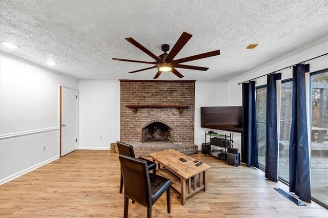 living room with ceiling fan, a brick fireplace, light hardwood / wood-style flooring, and a textured ceiling