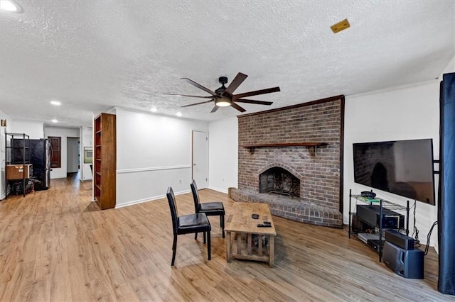 living room featuring a brick fireplace, a textured ceiling, ceiling fan, and light wood-type flooring