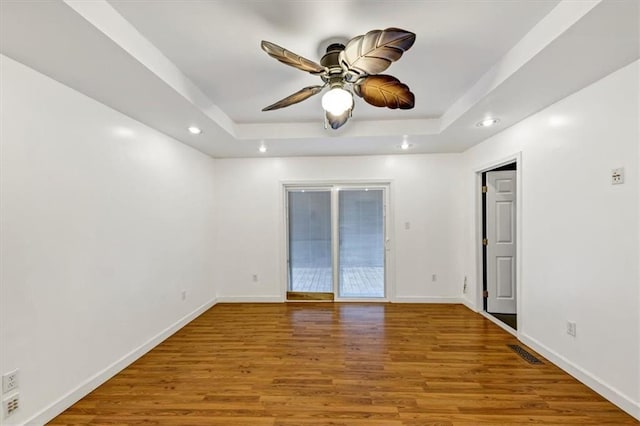 empty room featuring a raised ceiling, hardwood / wood-style floors, and ceiling fan