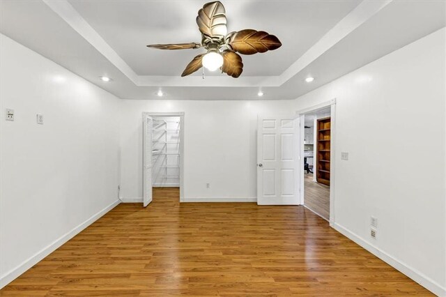 unfurnished room featuring ceiling fan, light hardwood / wood-style floors, and a tray ceiling