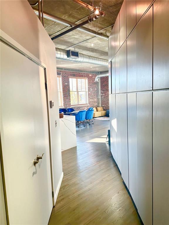 corridor featuring brick wall and light hardwood / wood-style flooring