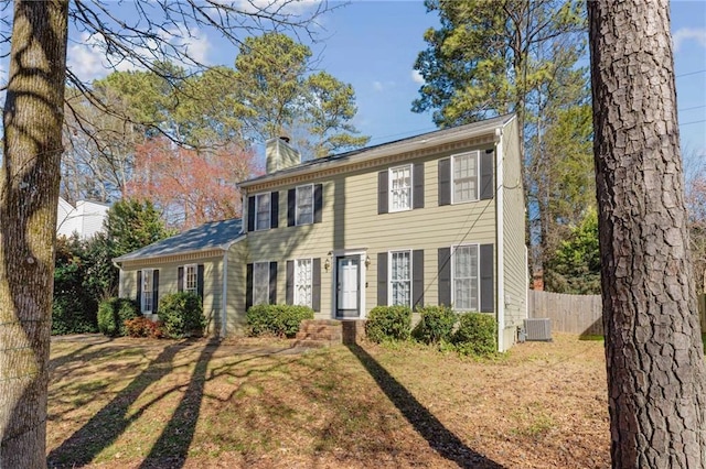 colonial home with a chimney, fence, and central AC