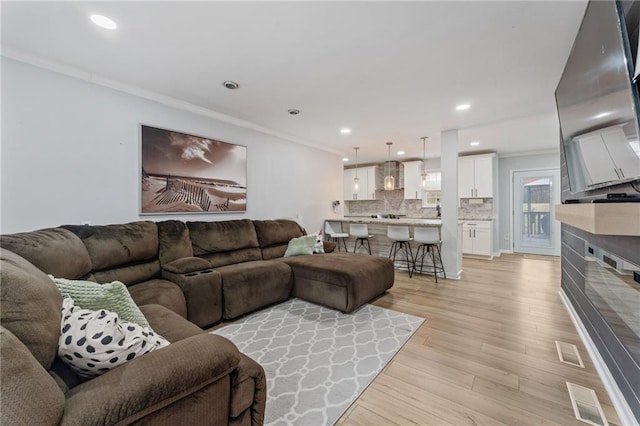 living room featuring crown molding, recessed lighting, visible vents, and light wood-style flooring