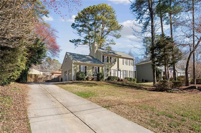 colonial-style house with a chimney, fence, a front yard, and concrete driveway